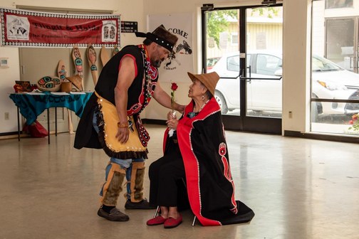 Southeast Alaska Native American man presenting rose to seated elderly Native American woman.