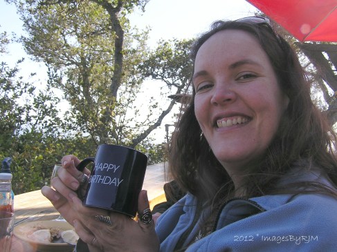 Smiling young woman holding "Happy Birthday" coffee mug.