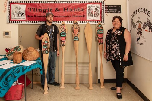 Young man and his mother standing beside hand-crafted Southeast Alaska Native American cedar canoe paddles.