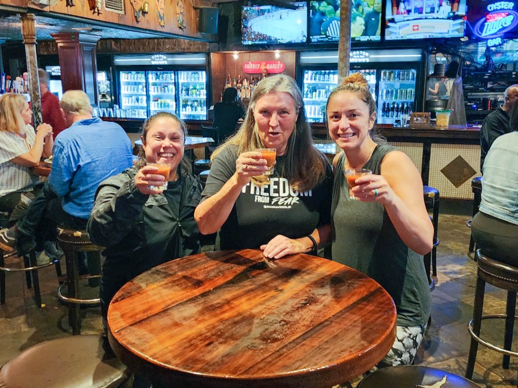 Image of three women, standing at table in a bar, holding raised shot glasses, at Cooter Brown's, New Orleans.