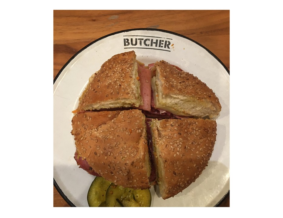Image of muffaletta sandwich, cut into four wedges, on a white plate marked "Butcher," taken at Cochon Butcher in New Orleans.

