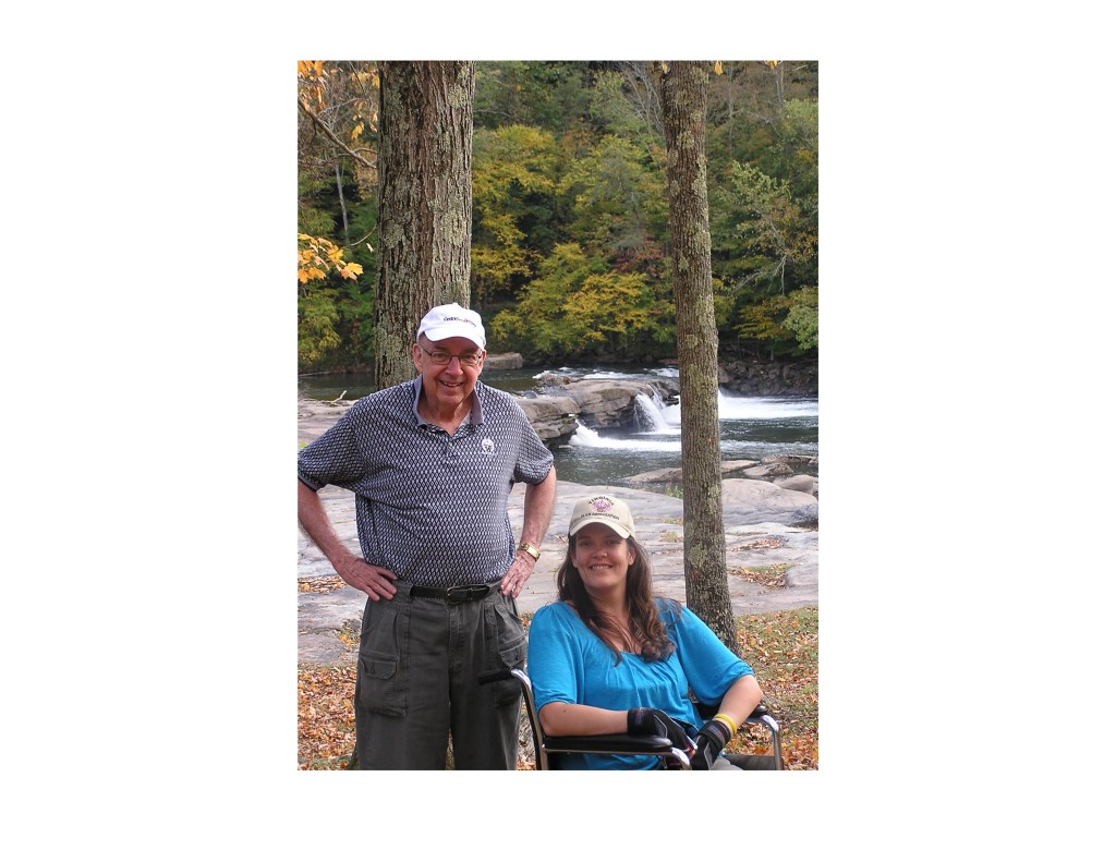 Image of standing man and seated young woman, with water and trees in the background. Taken in West Virginia.