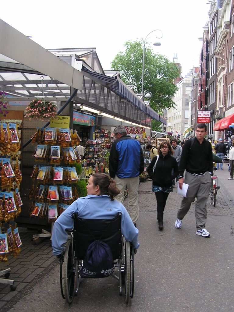Young woman in wheelchair looking at seed packets and bags of tulip bulbs at Bloemenmarkt, Amsterdam.