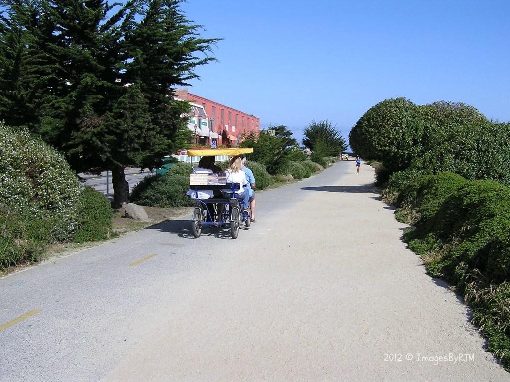 People pedaling a canopied quadricycle along Monterey Bay Coastal Trail.