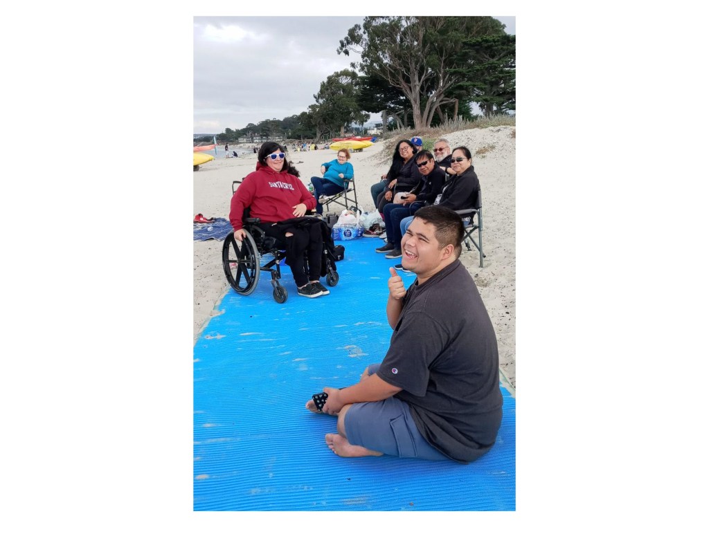 Family on ADA beach mat, including woman in wheelchair, at Del Monte Beach, Monterey, California.
